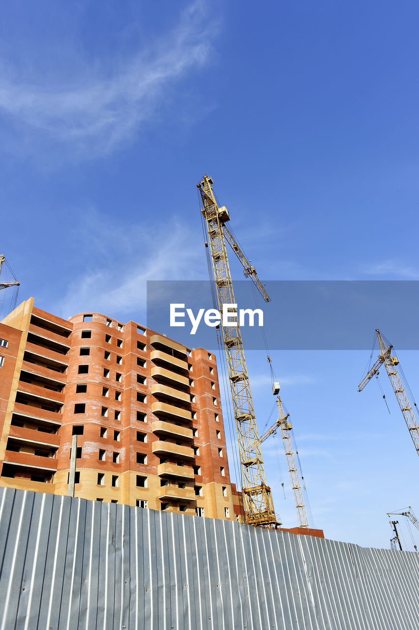 Low angle view of crane by buildings against blue sky