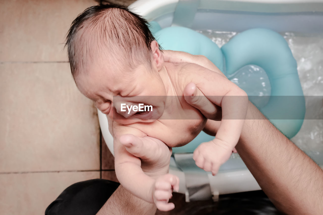 A baby is crying while the father to give him a bath