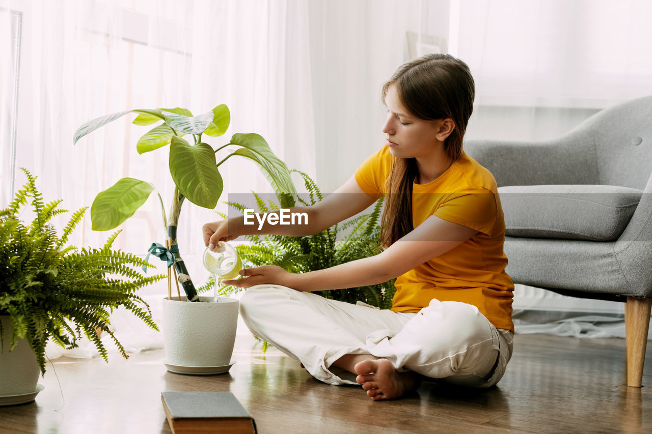 A young happy girl is watering potted plants with water in her small home garden. 