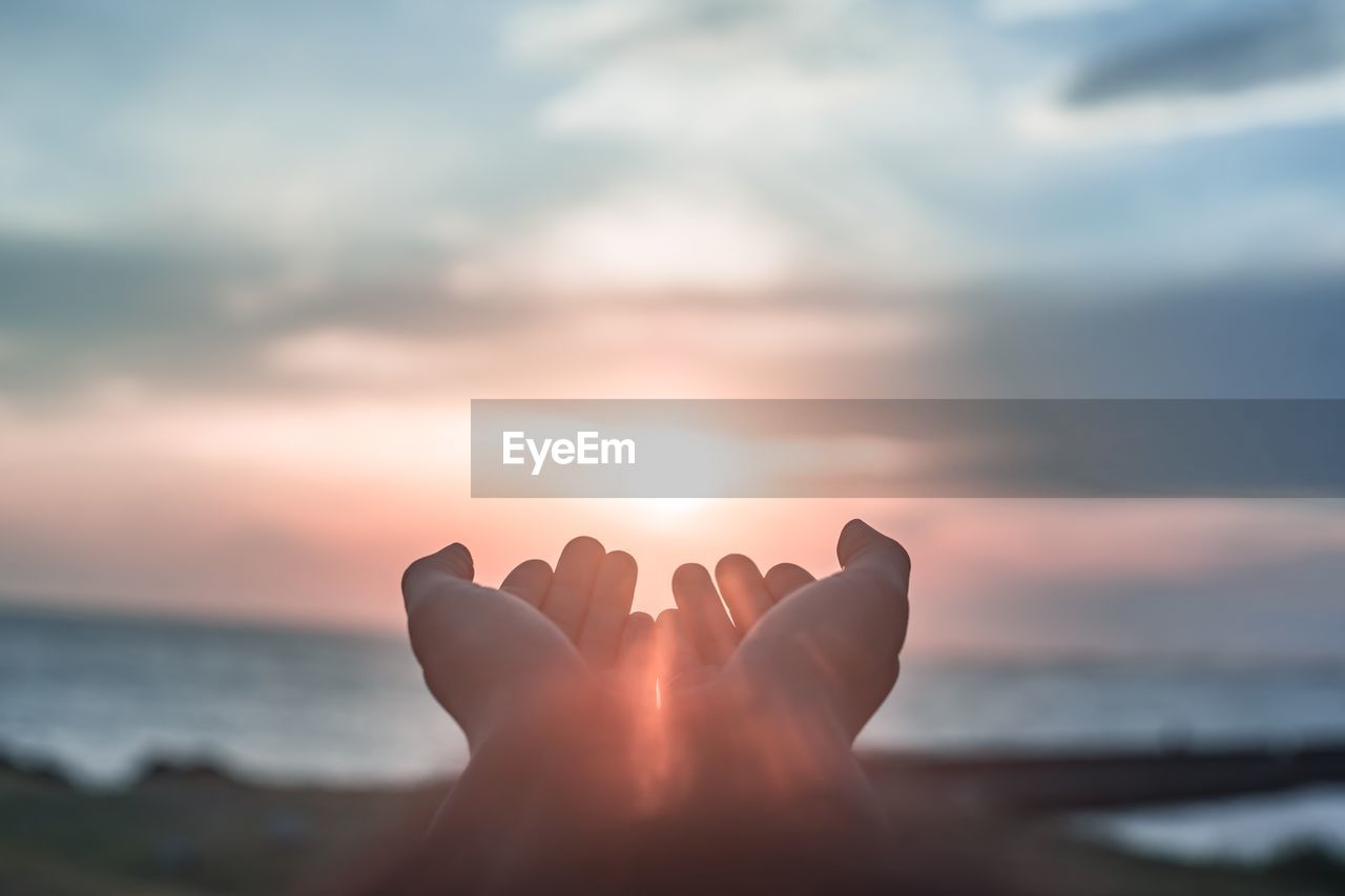 Cropped hands against sea during sunset