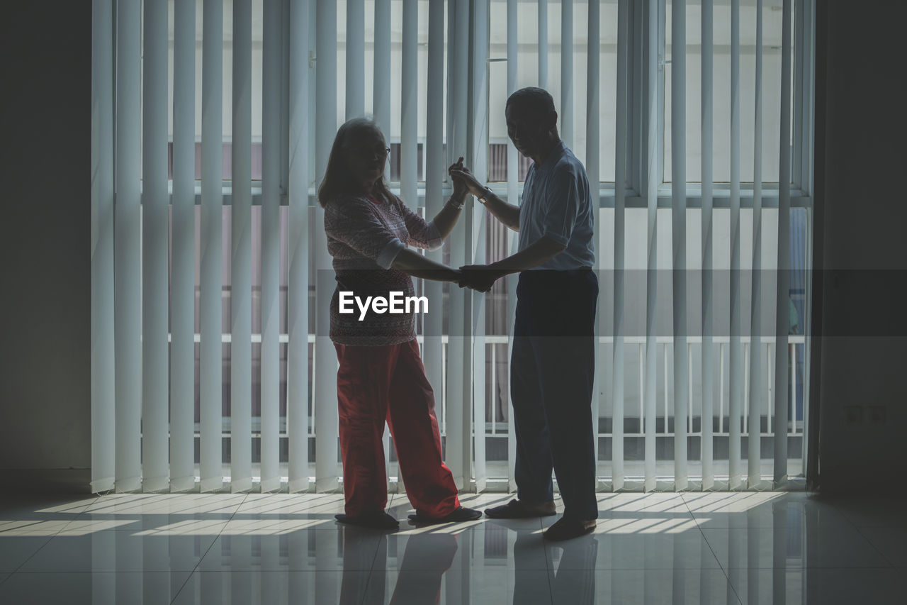 Senior couple dancing on floor by window