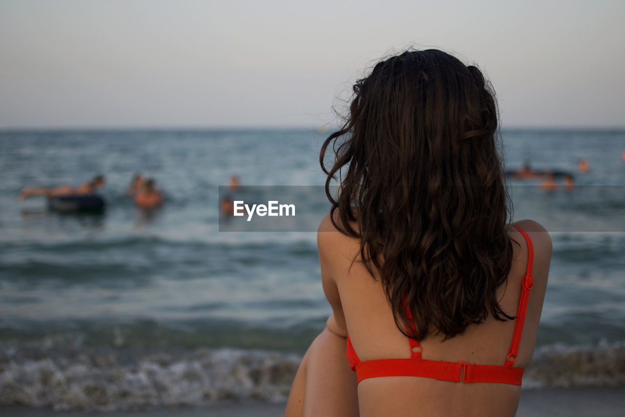 Rear view of woman at beach against sky