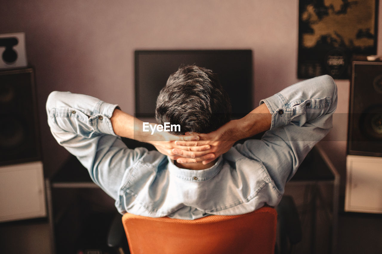 Man relaxing sitting on chair by computer with hands behind head