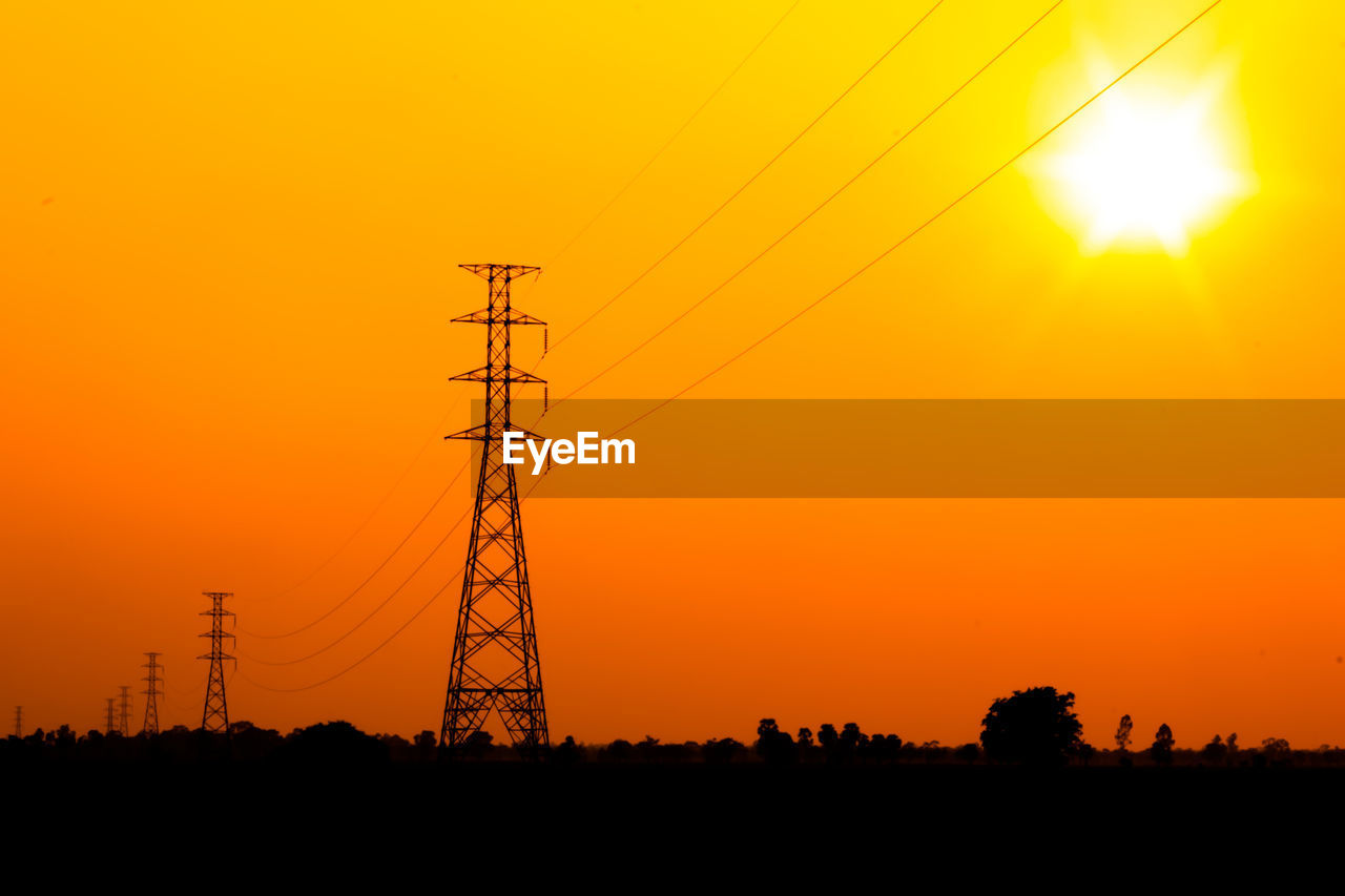 Silhouette electricity pylon against orange sky