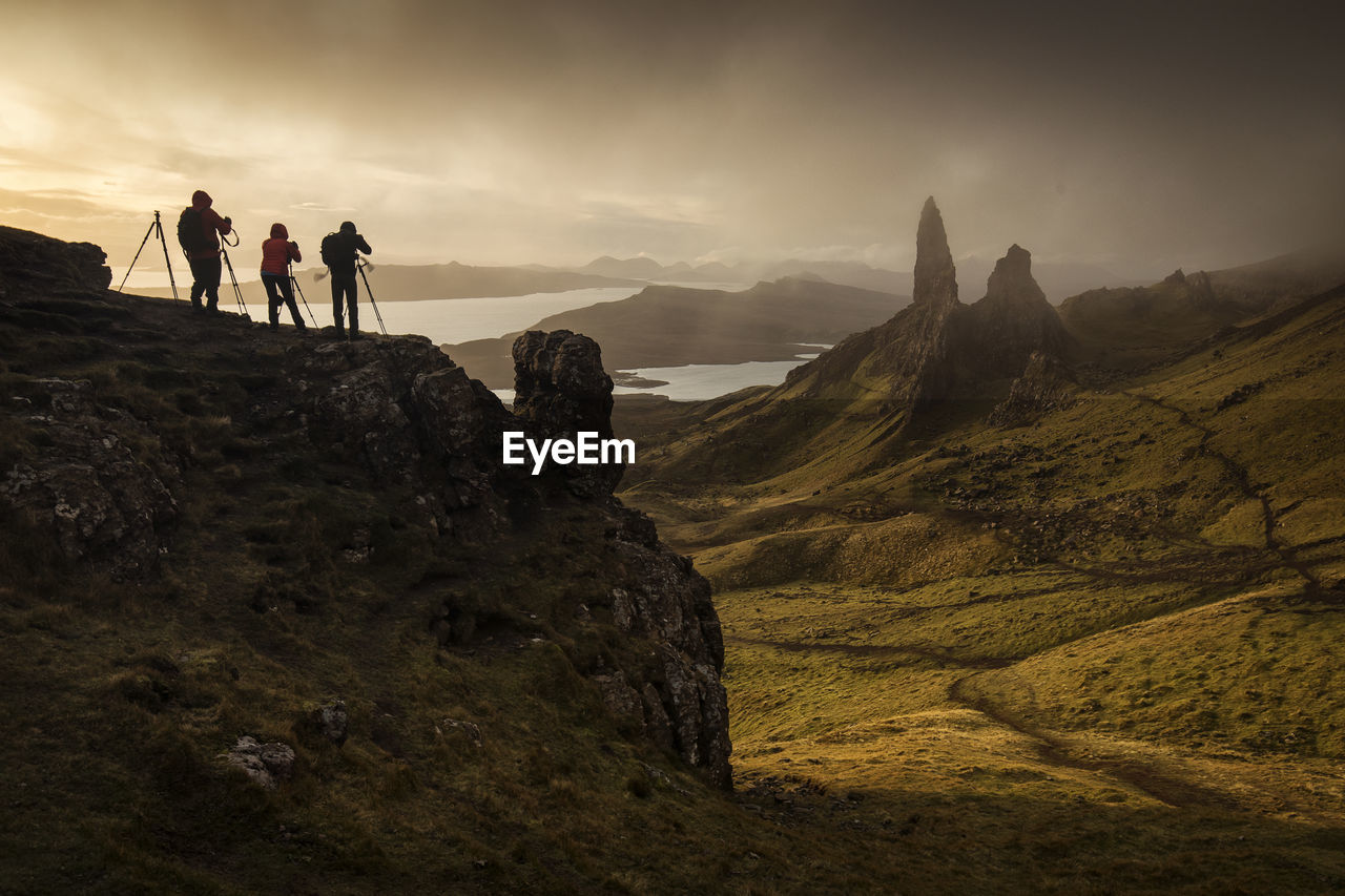 Hikers photographing while standing on cliff against sky