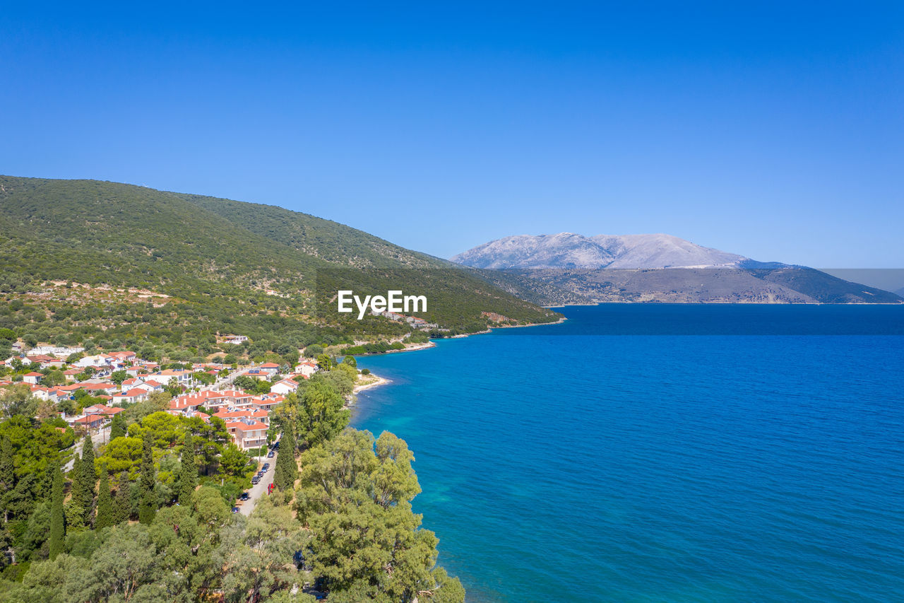 High angle view of townscape by sea against clear blue sky