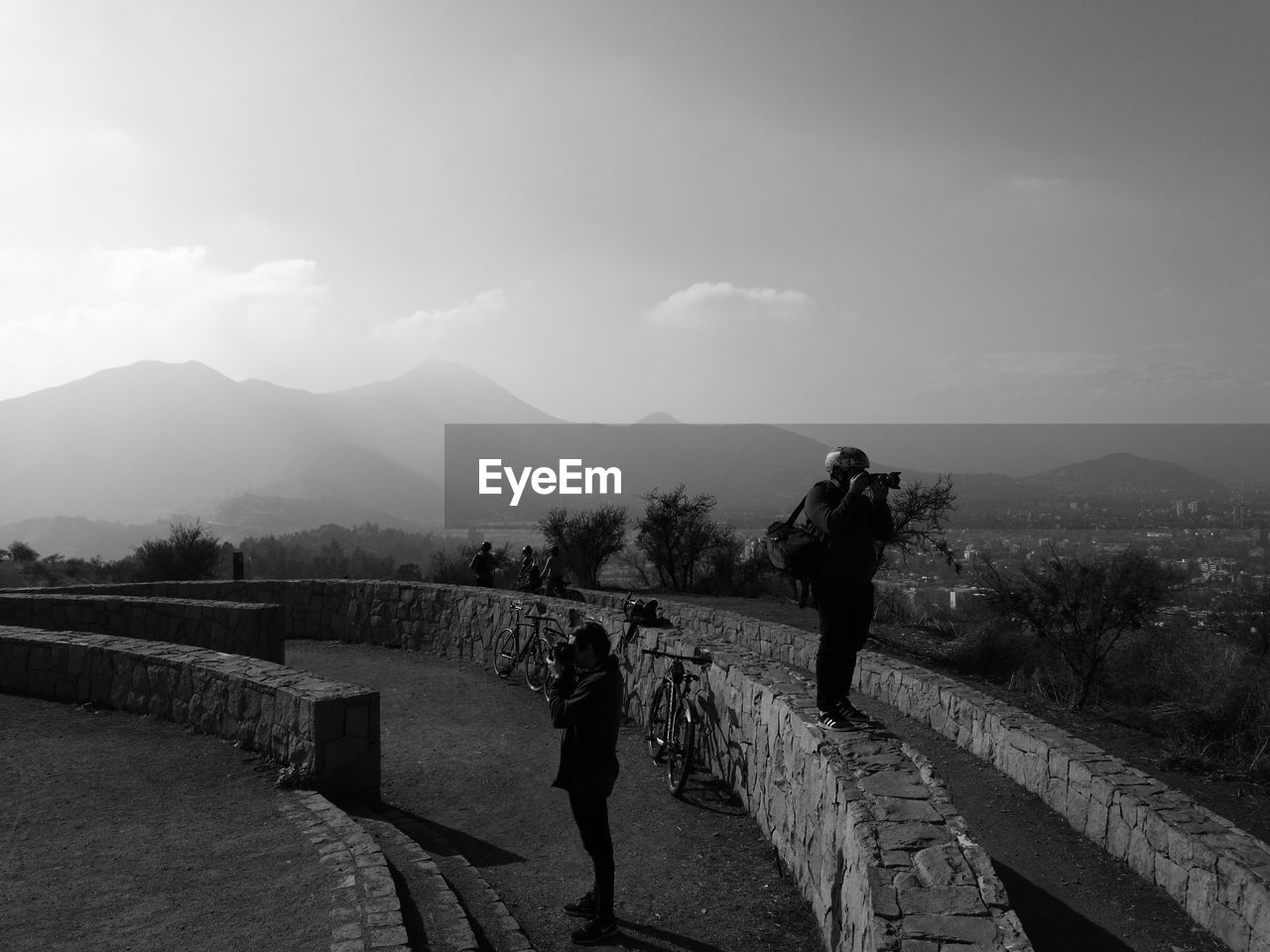 REAR VIEW OF PEOPLE STANDING ON RAILING AGAINST MOUNTAIN