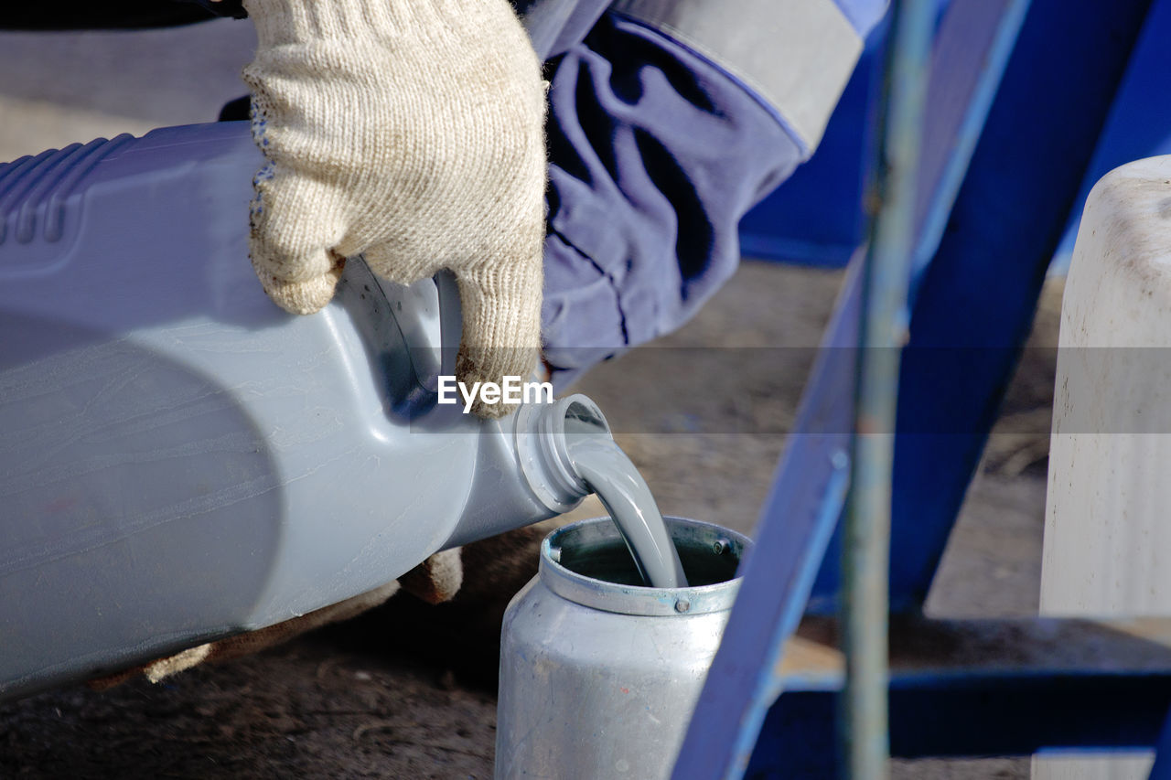 A gloved worker pours gray paint from a canister into a spray gun. preparation for painting works.