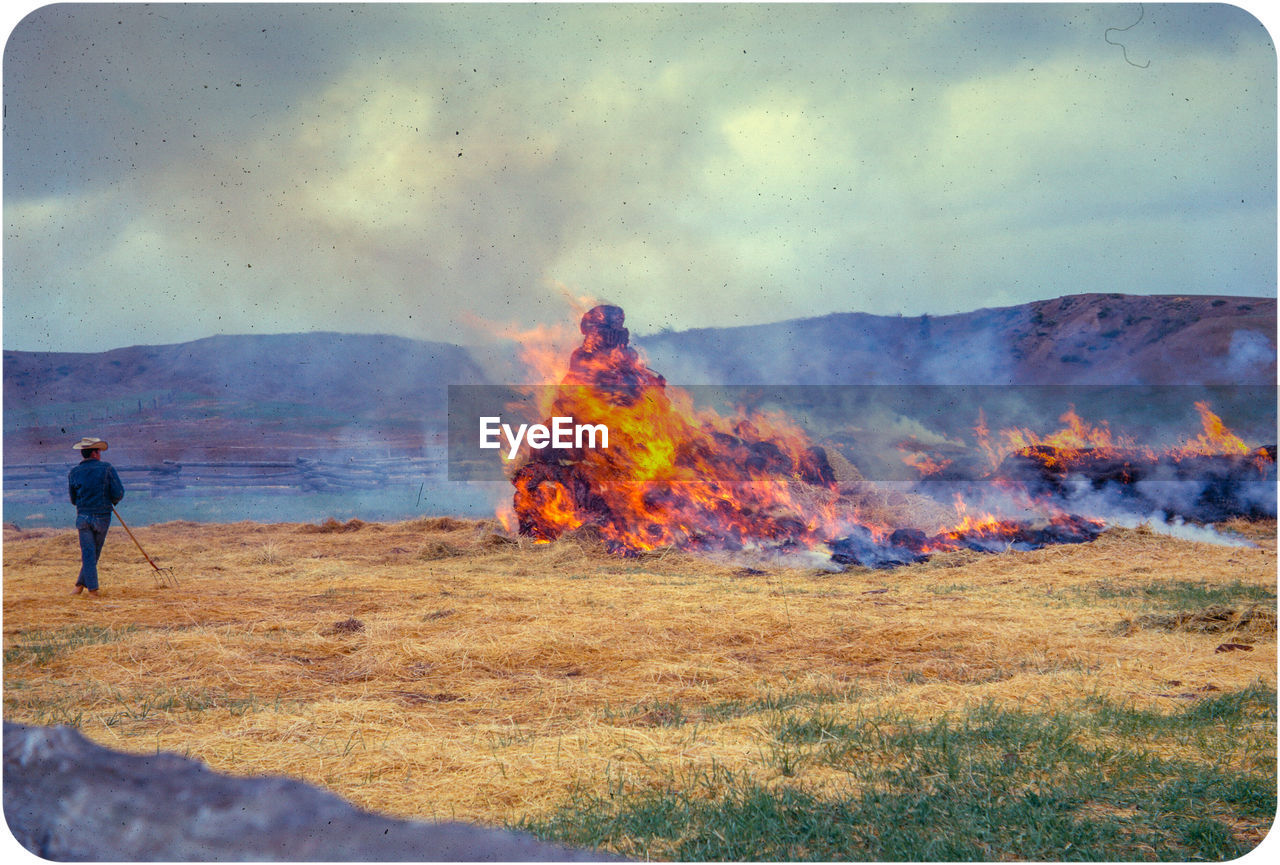 Full length of man standing by burning straw against sky