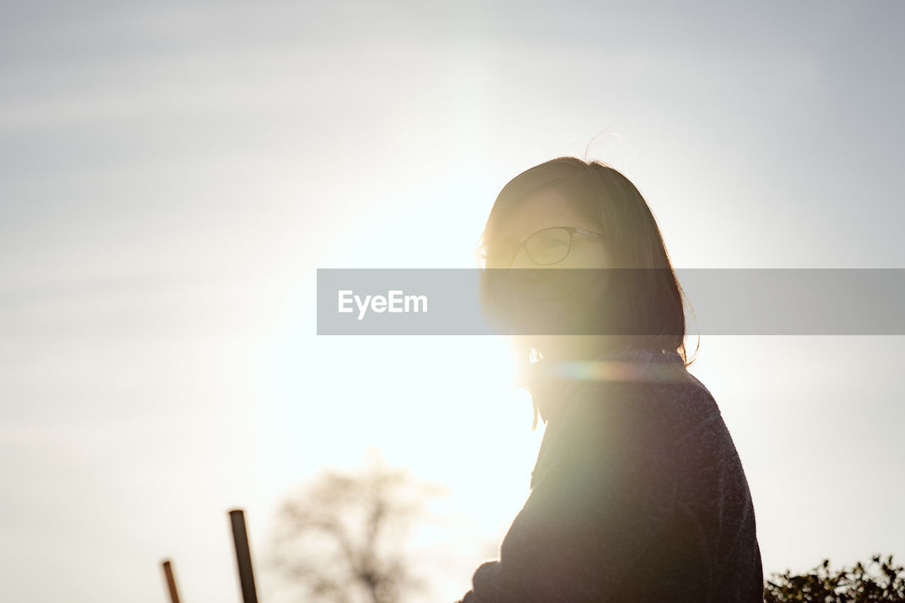 Low angle view of woman against bright sun during sunset