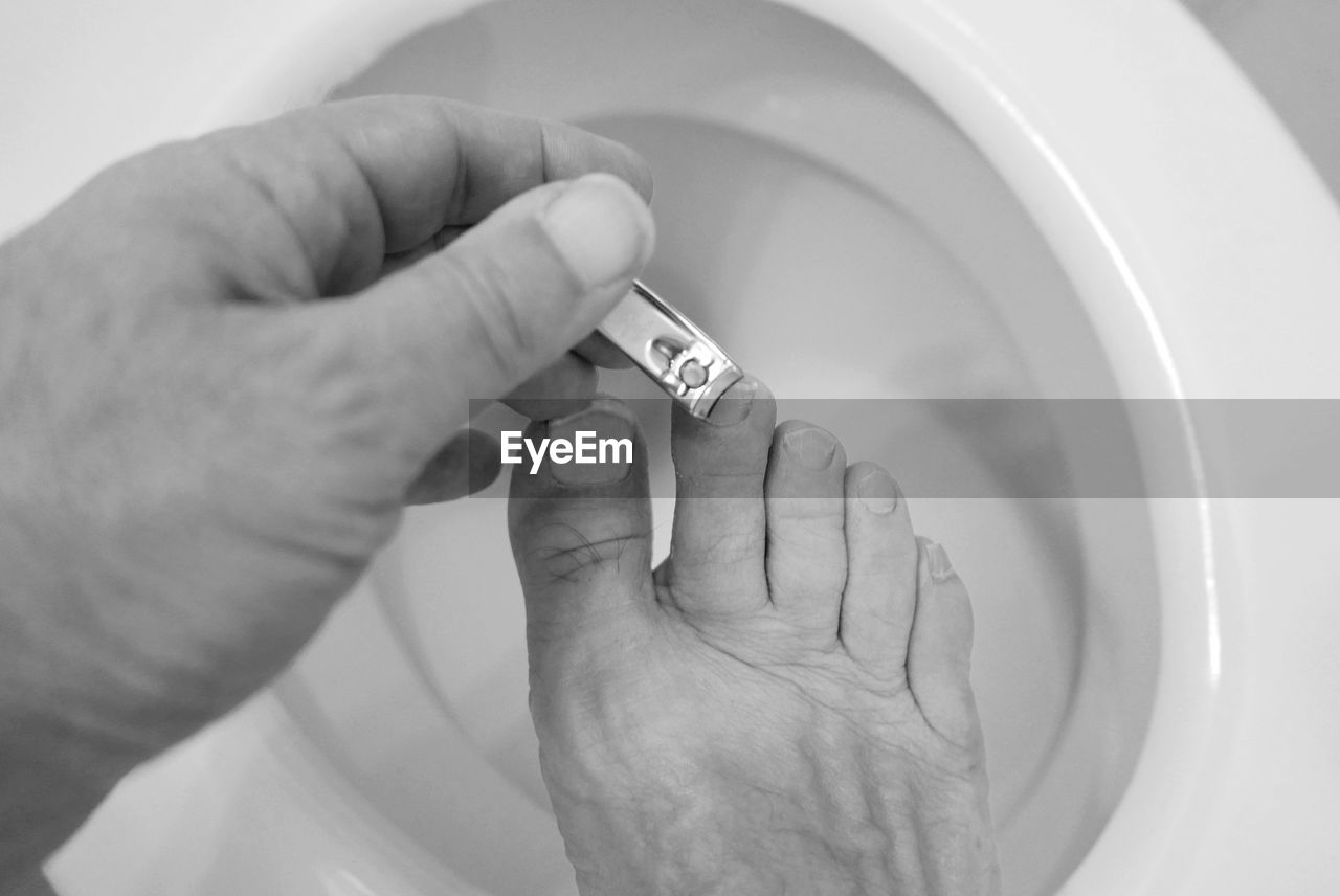 Man clipping toenails on toilet commode
