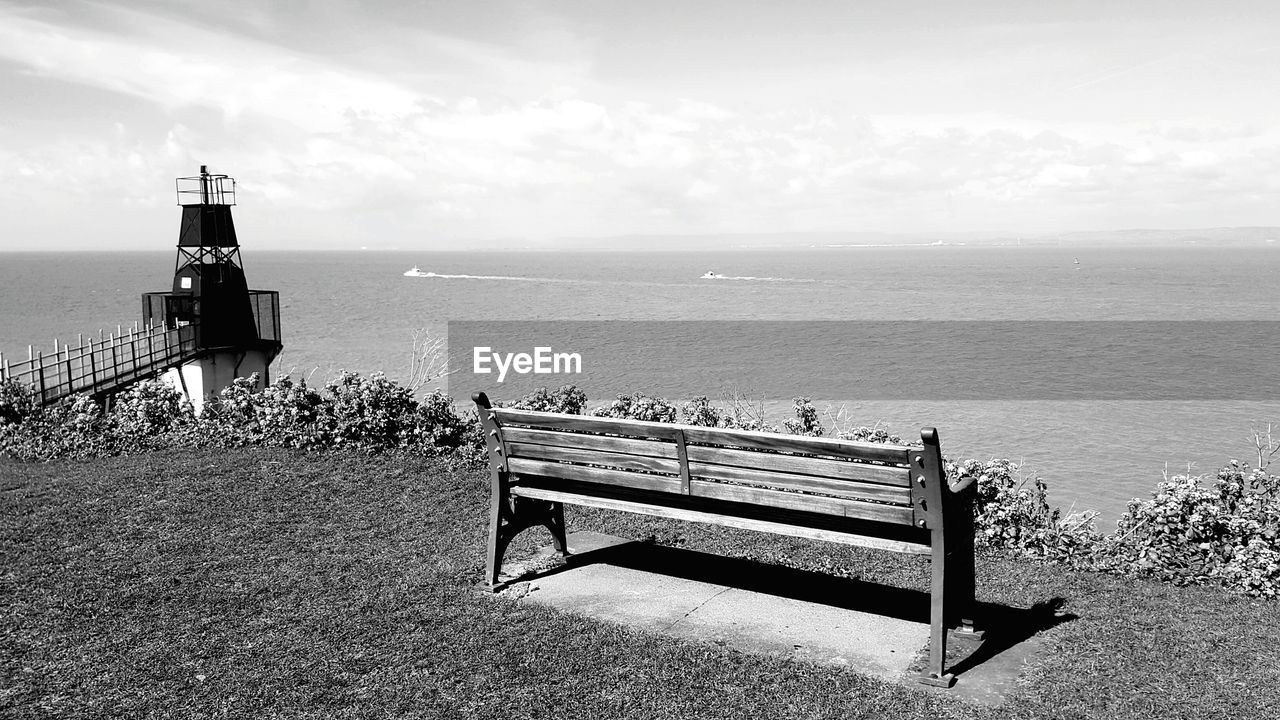 Empty bench on field by sea against sky