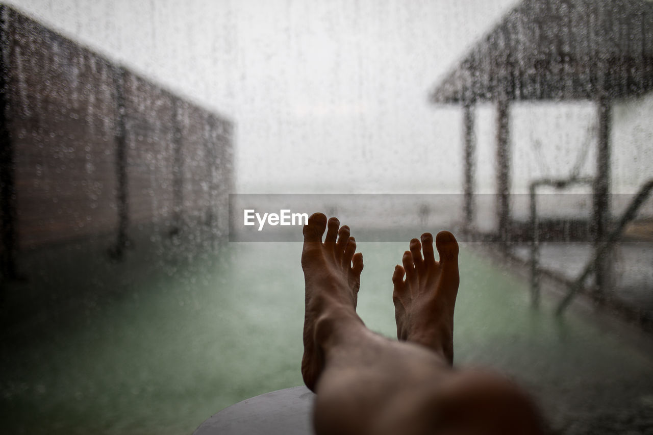 Low section of person relaxing against window during rainy season