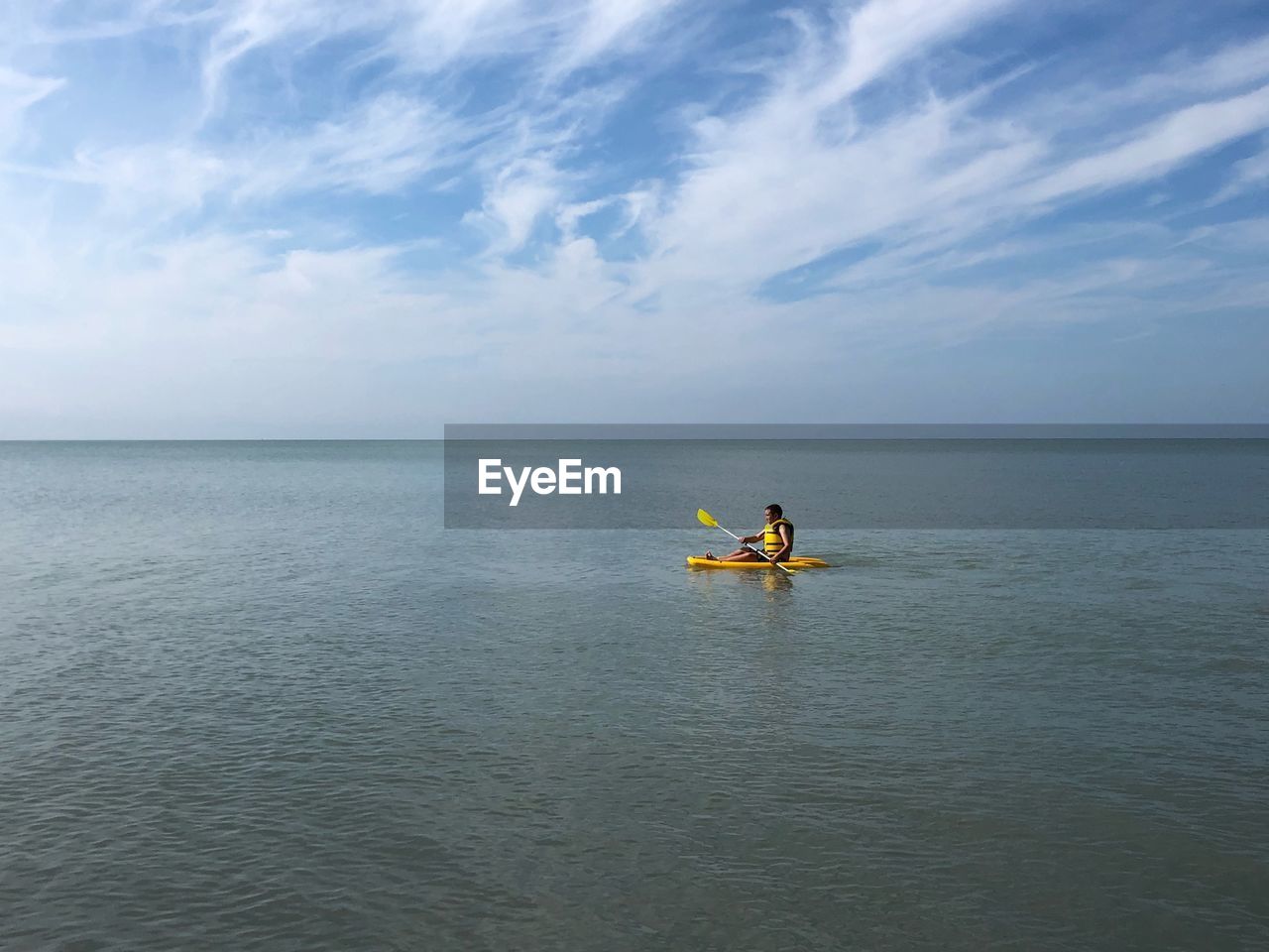 Boy rowing kayak in sea against sky