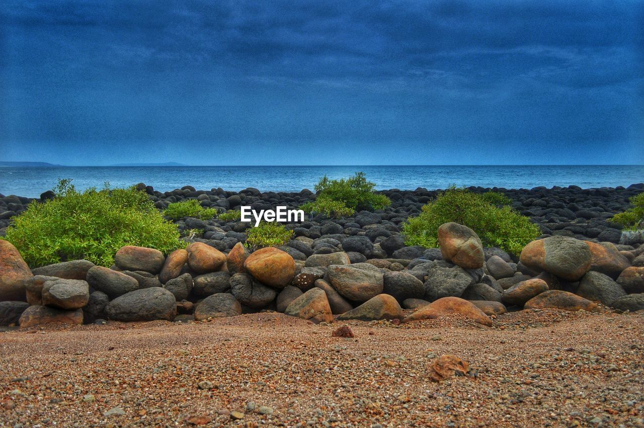 SCENIC VIEW OF ROCKY BEACH AGAINST CLOUDY SKY