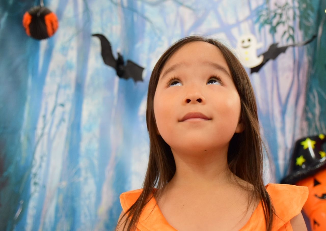 Low angle view of girl looking up against halloween decoration on wall