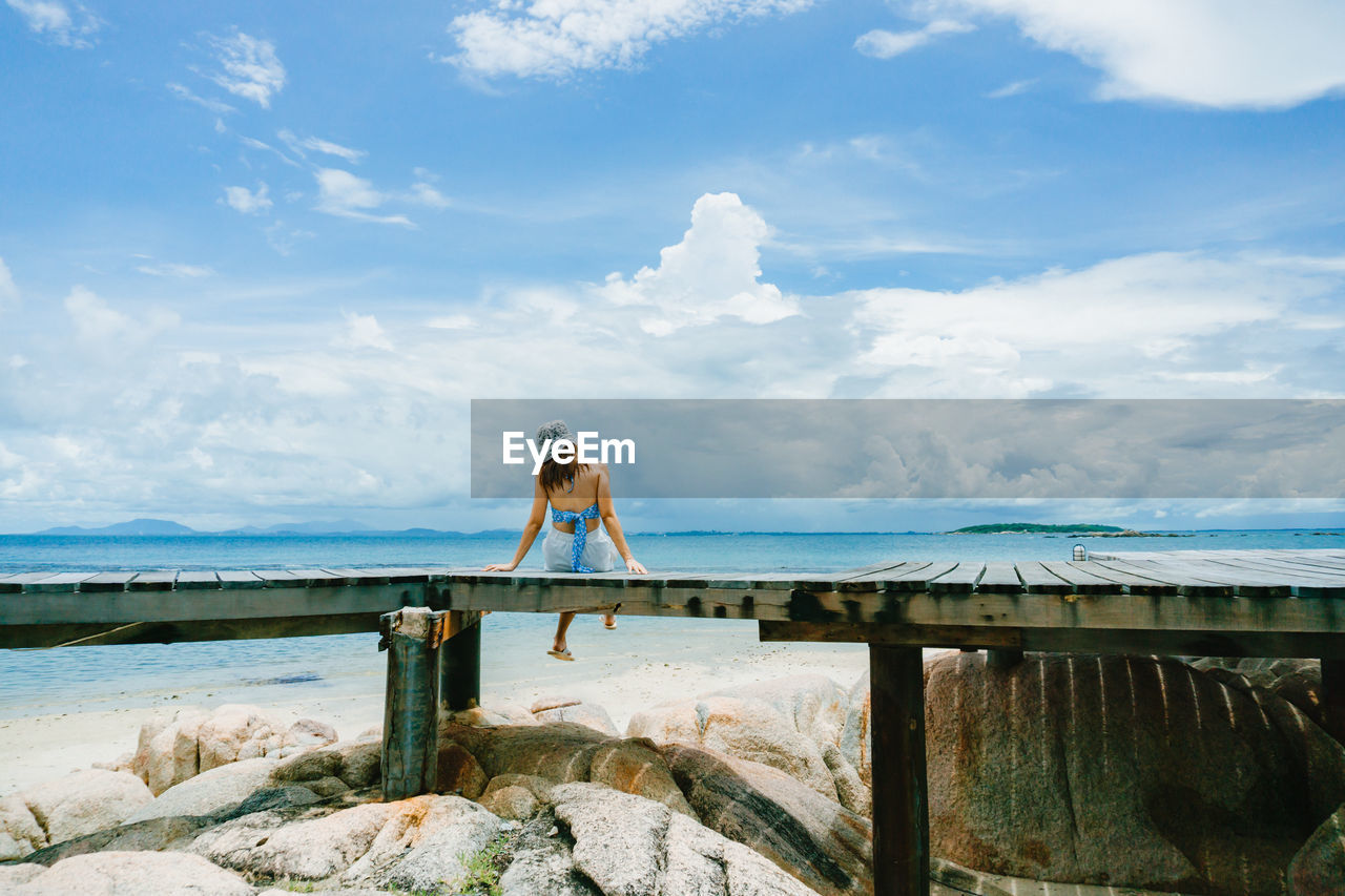 REAR VIEW OF WOMAN STANDING ON ROCK AGAINST SEA