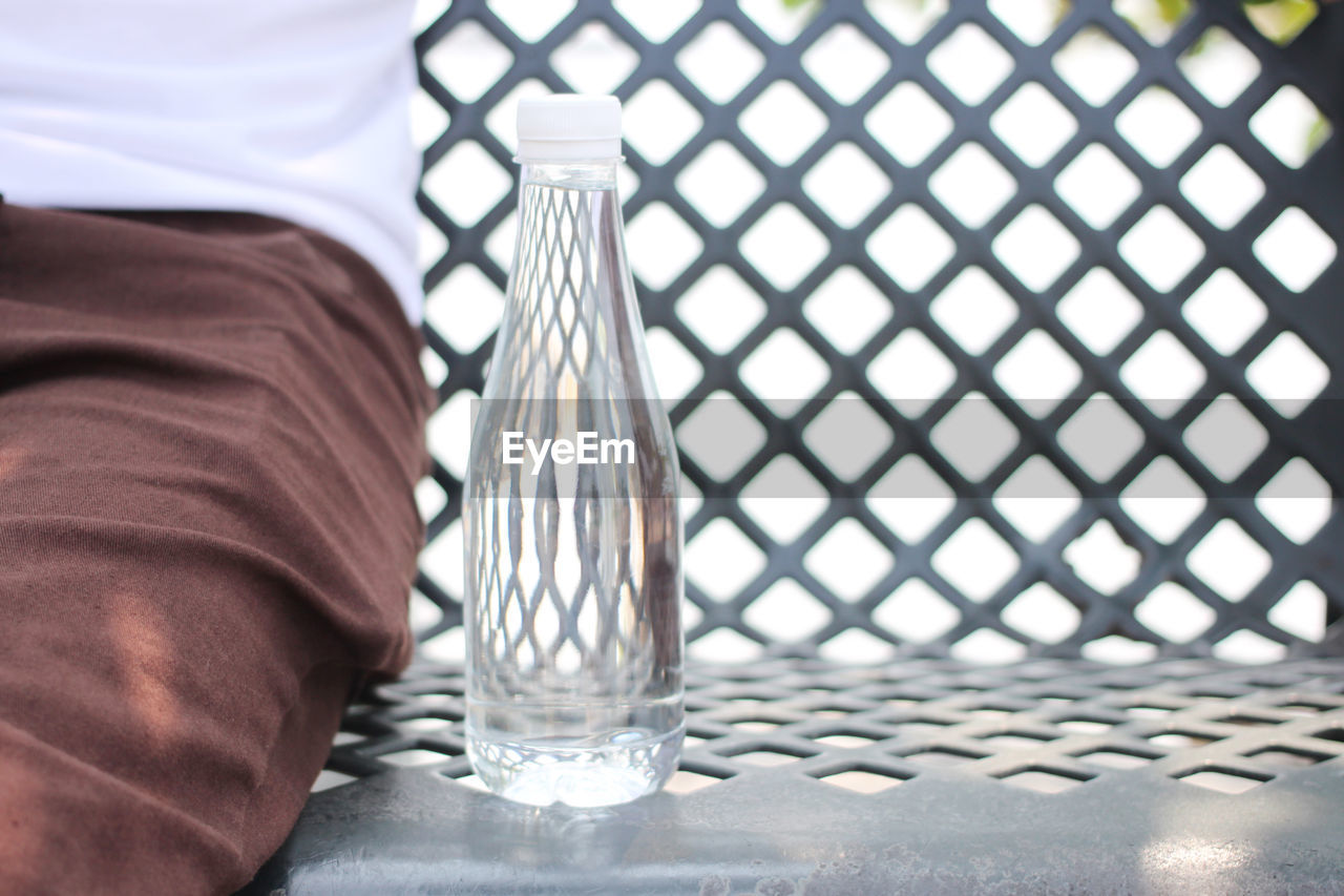 Midsection of man sitting by water bottle on bench