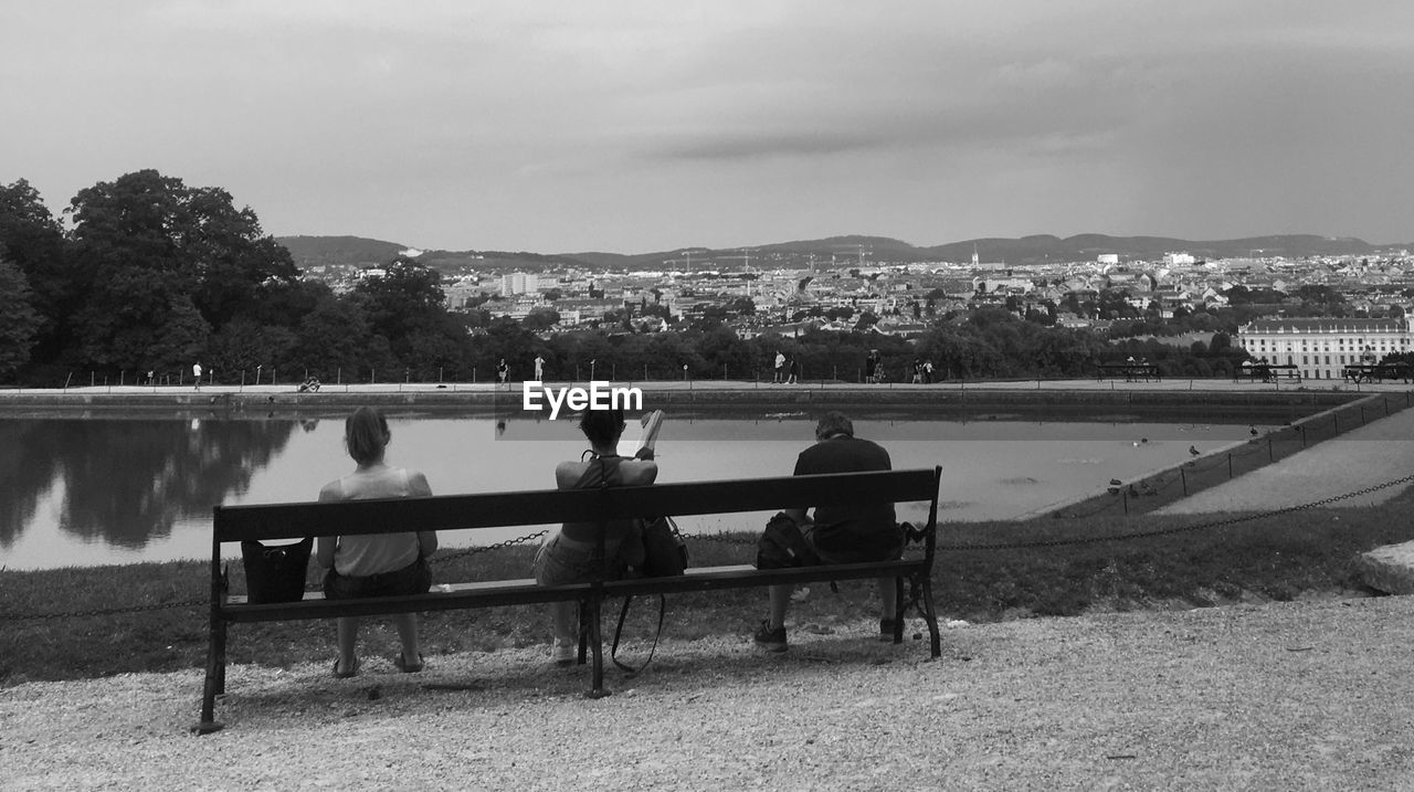 MEN SITTING ON BENCH BY LAKE AGAINST SKY