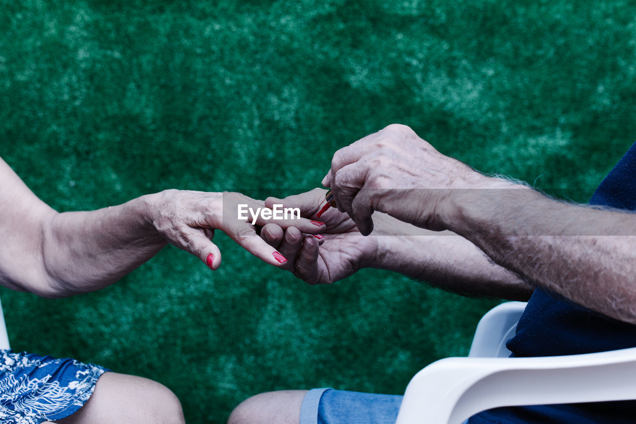 Old man painting his wife's nails red sitting on a chair