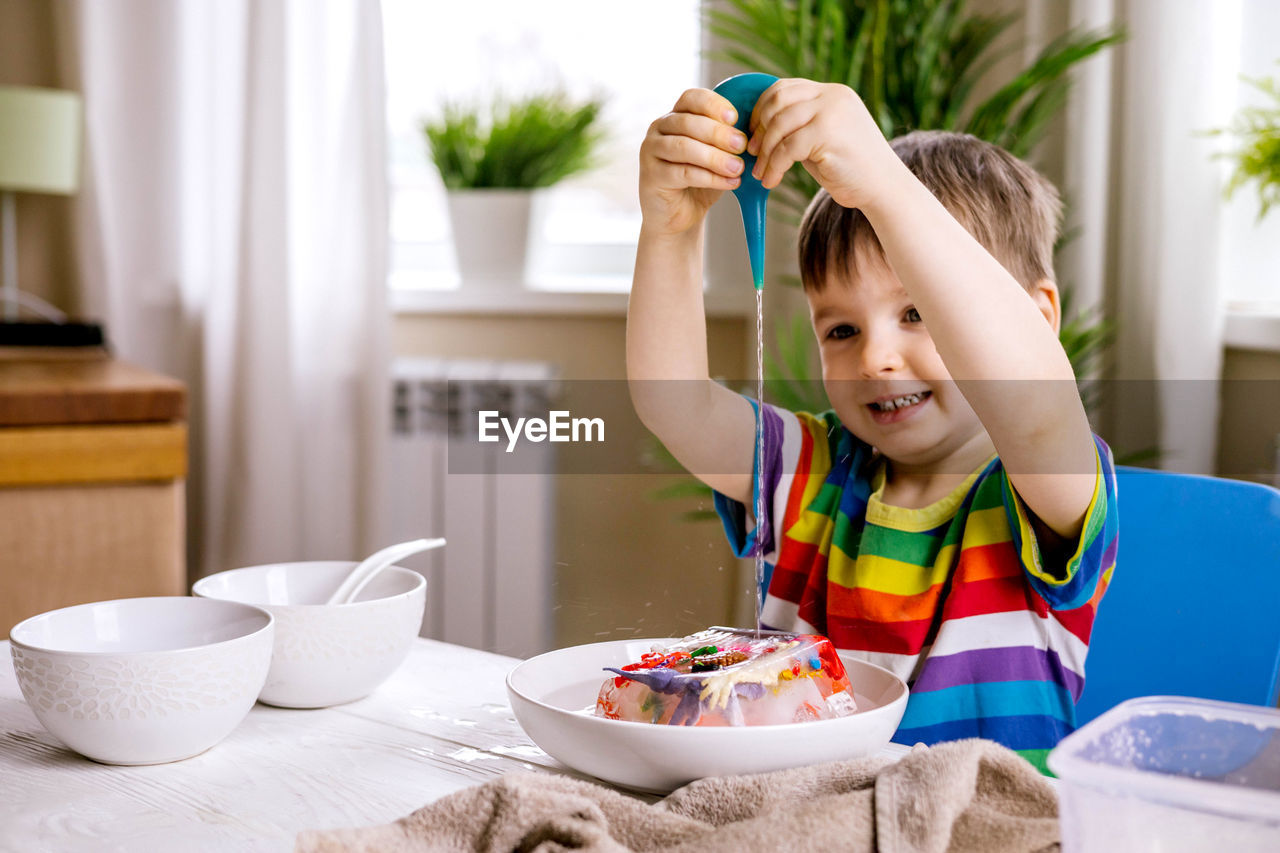 Smiling boy pouring water on frozen toys at home