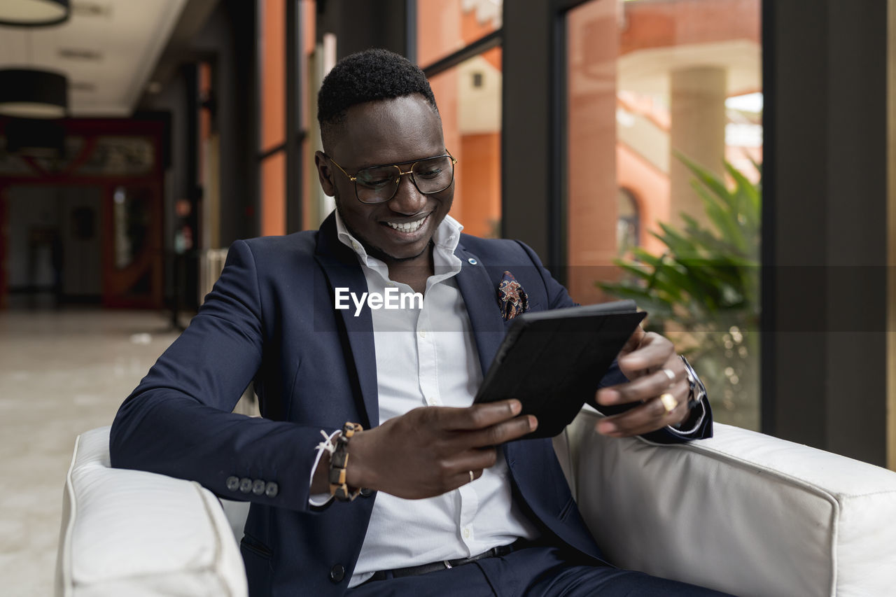 Smiling male entrepreneur using digital tablet while sitting in hotel lobby