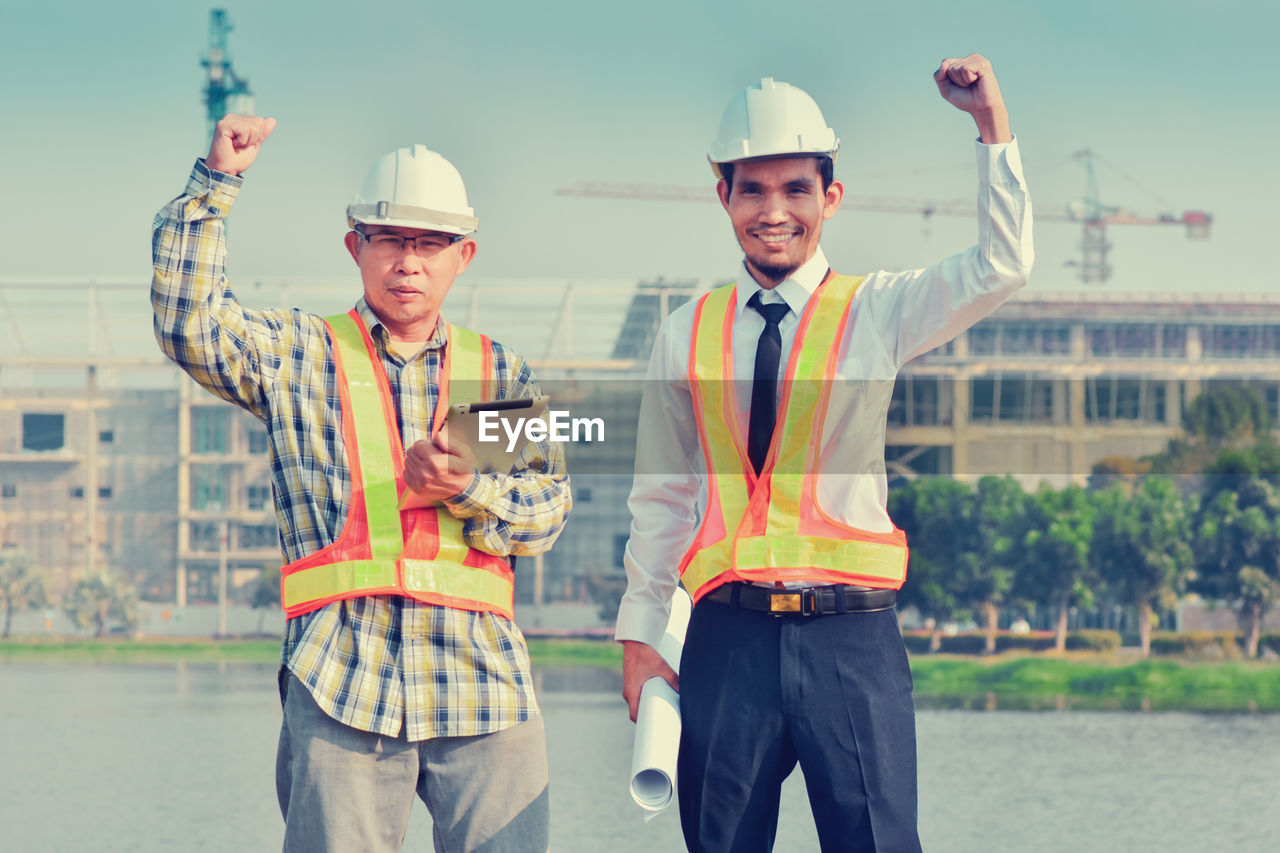 YOUNG MAN WORKING ON CONSTRUCTION SITE WITH ARMS RAISED
