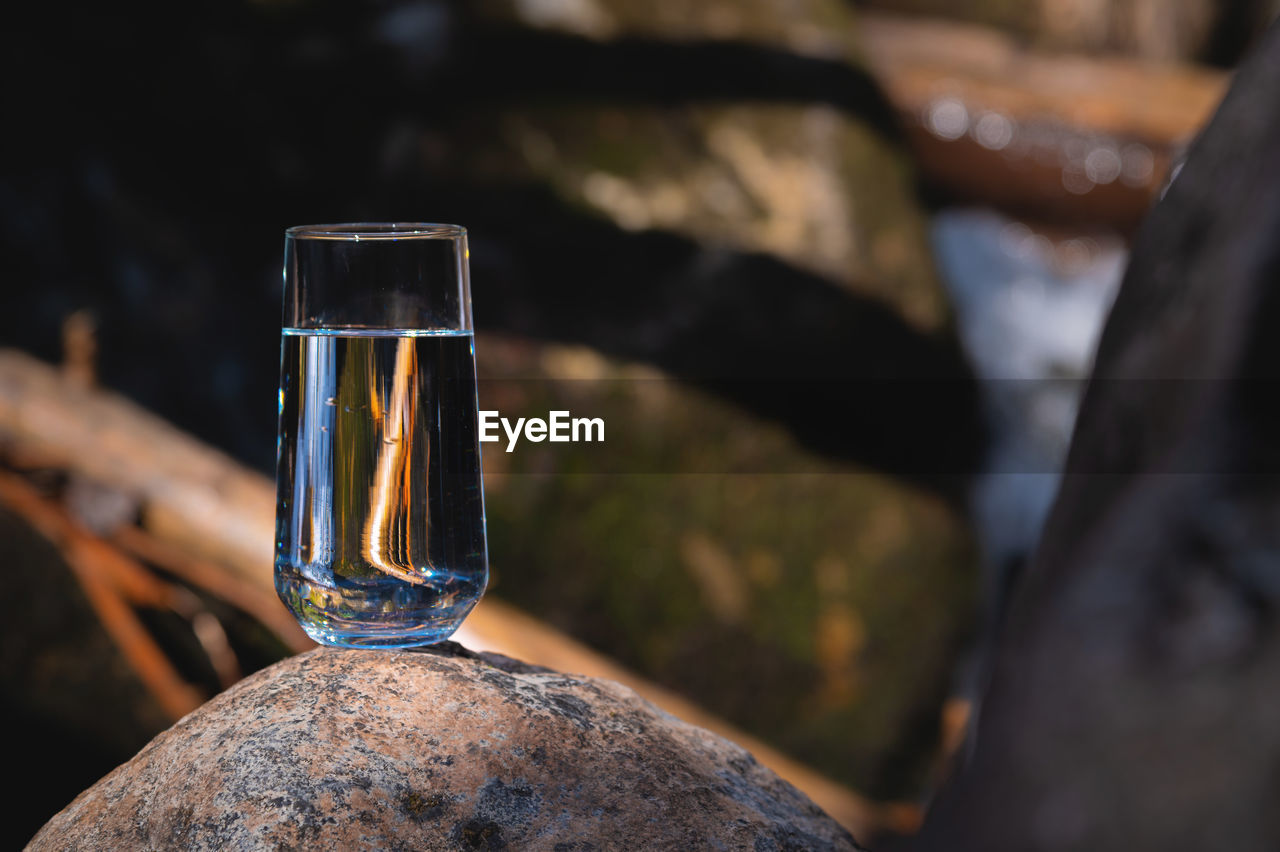 Glass of water on stones and a river in the background. nature blur background