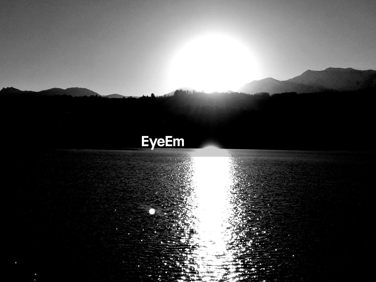 REFLECTION OF SUN IN WATER ON SILHOUETTE OF ROCKS