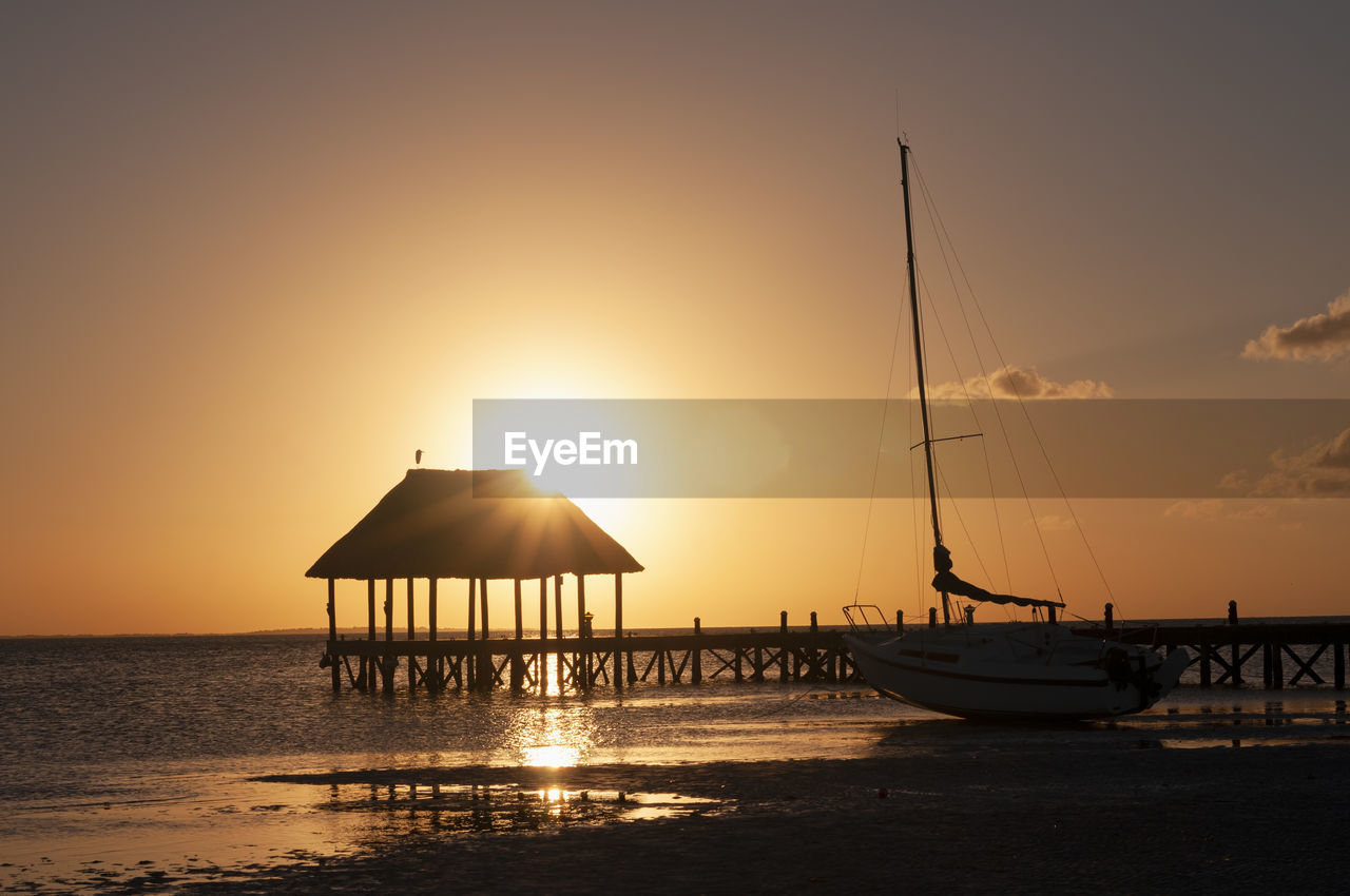 A wooden pier on the sea at sunset and a sailing boat on the beach in holbox island in mexico