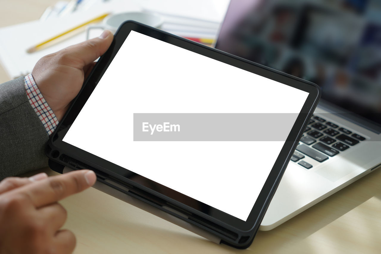 Cropped hands of businessman using blank digital tablet at desk