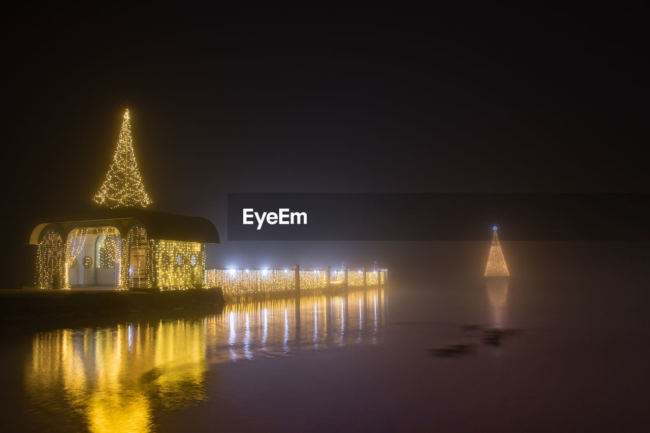 ILLUMINATED TEMPLE BY LAKE AT NIGHT