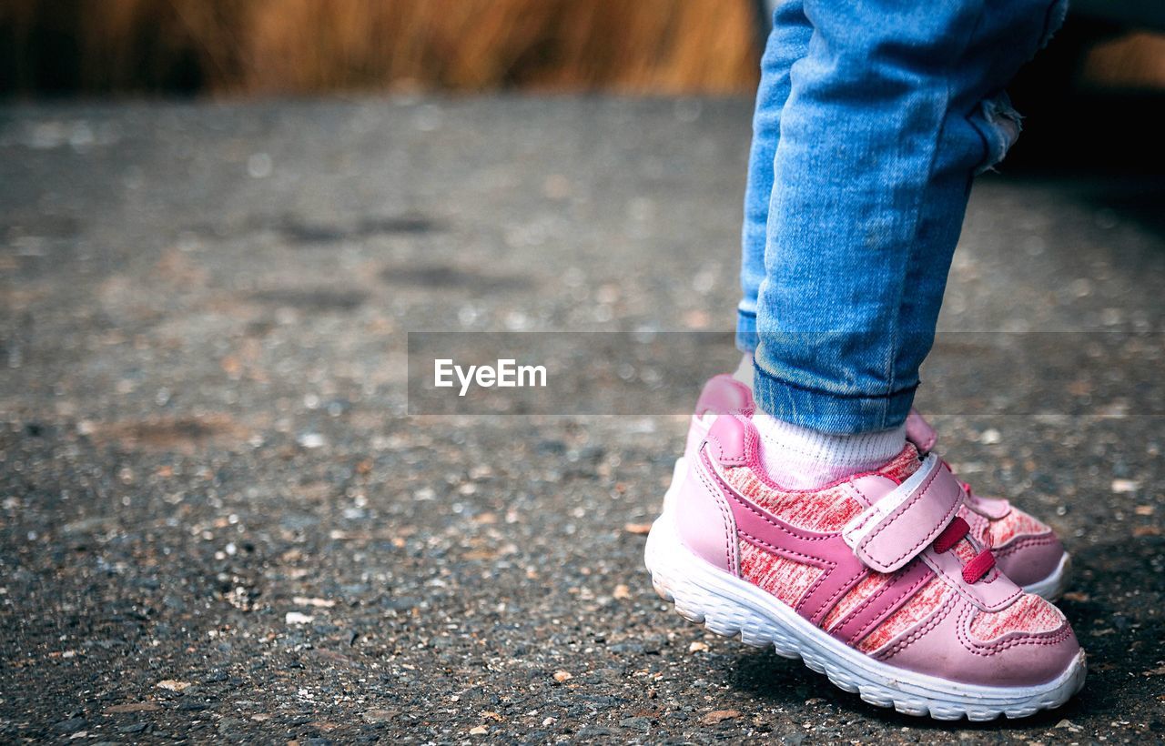 Low section of baby girl wearing pink shoes while standing on footpath