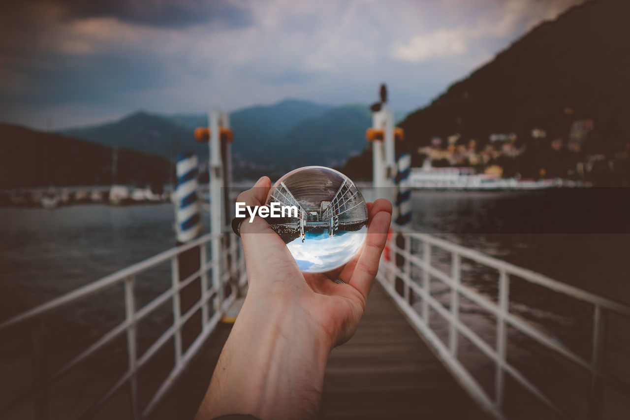 Cropped hand holding crystal ball against lake