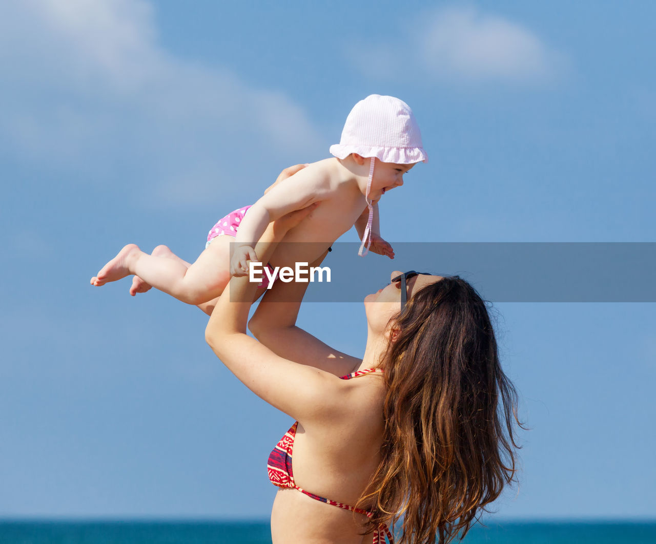 Mother holding cute daughter against sky