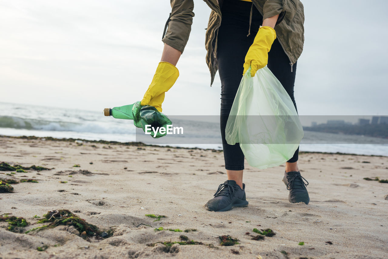 Environmentalist with garbage bag cleaning beach while standing against clear sky