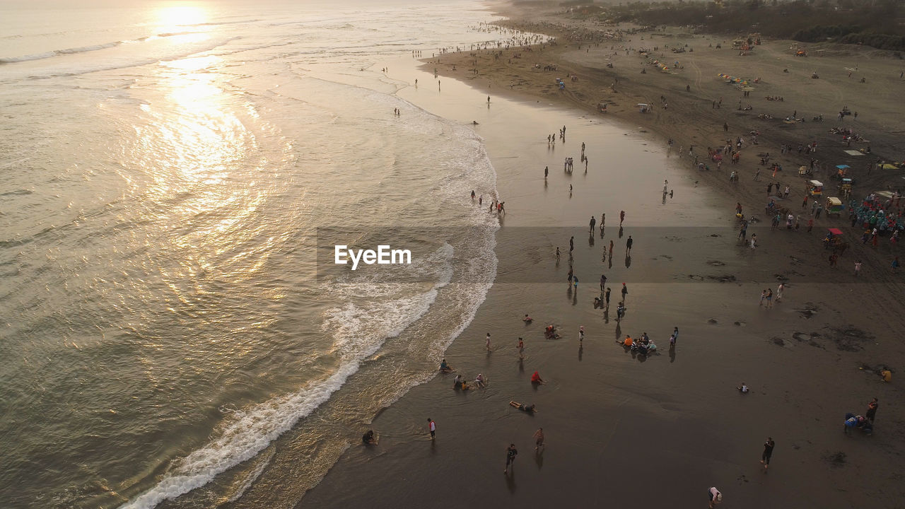 Sandy beach parangtritis near ocean with big waves, people in tropical resort at sunset. yogyakarta