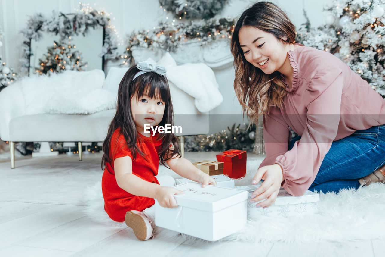 Portrait of cute girl with mother sitting by christmas gift