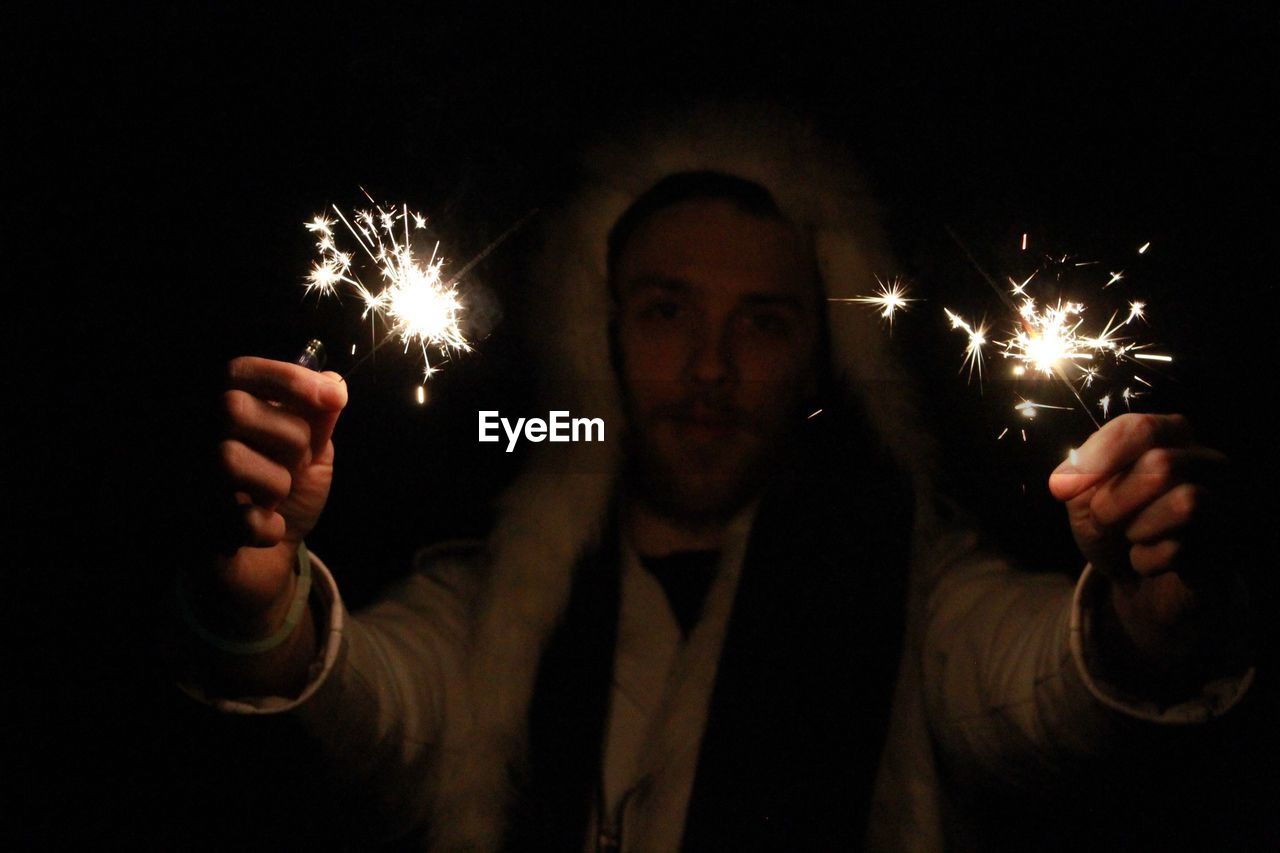 Portrait of man holding illuminated sparklers at night