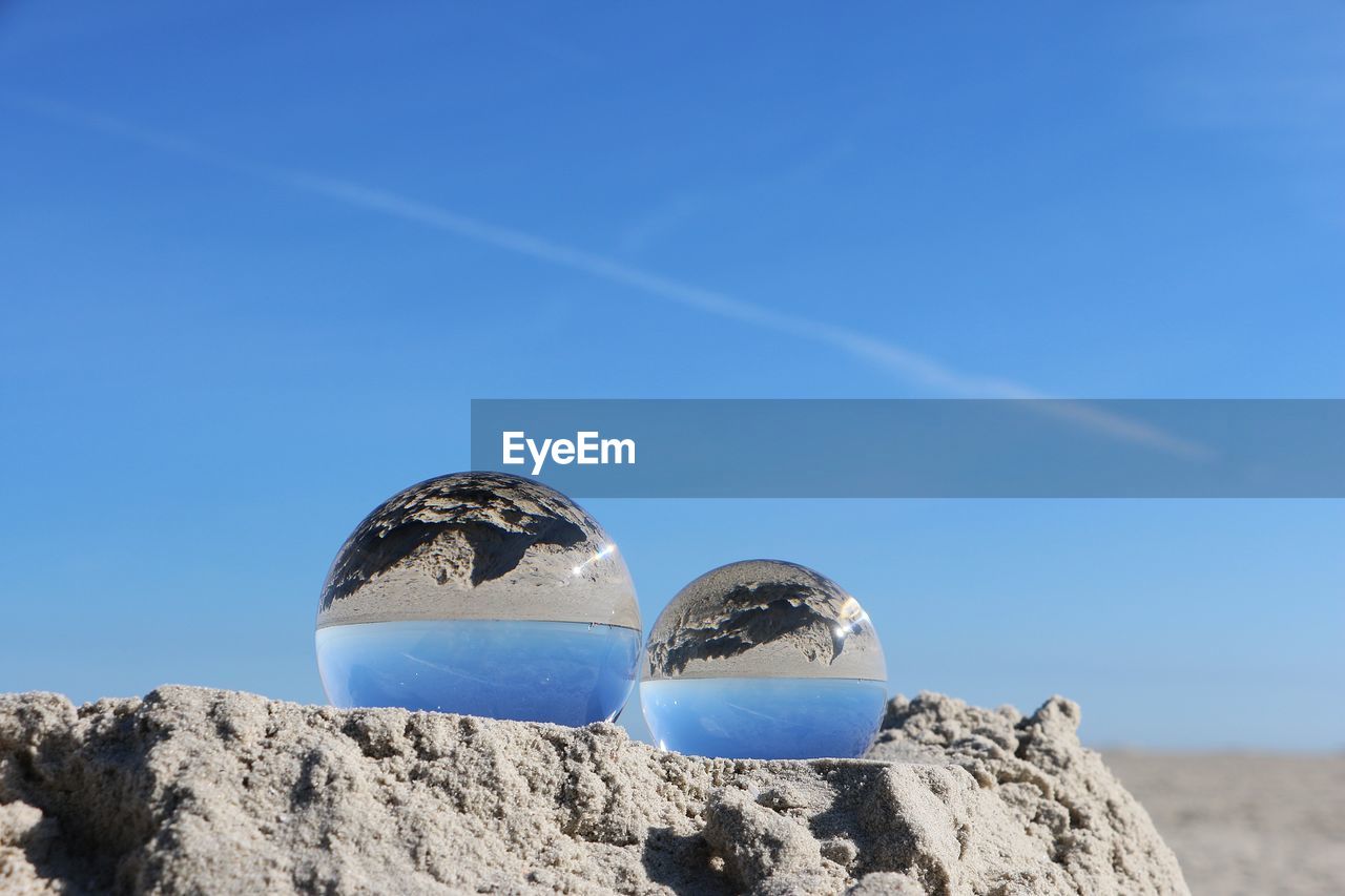 Crystal balls on sand against sky