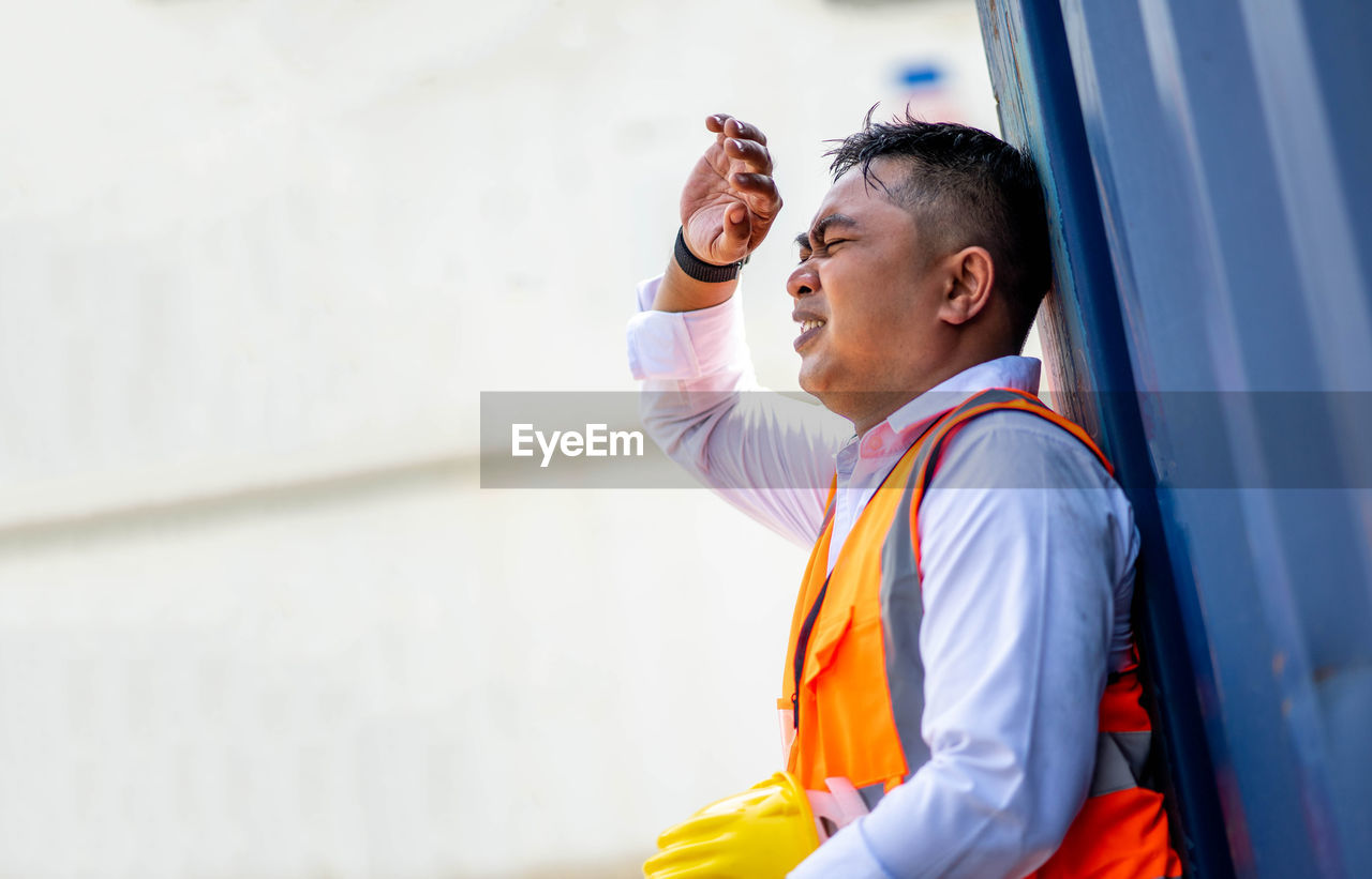 SIDE VIEW OF MAN LOOKING AWAY WHILE STANDING AGAINST WALL