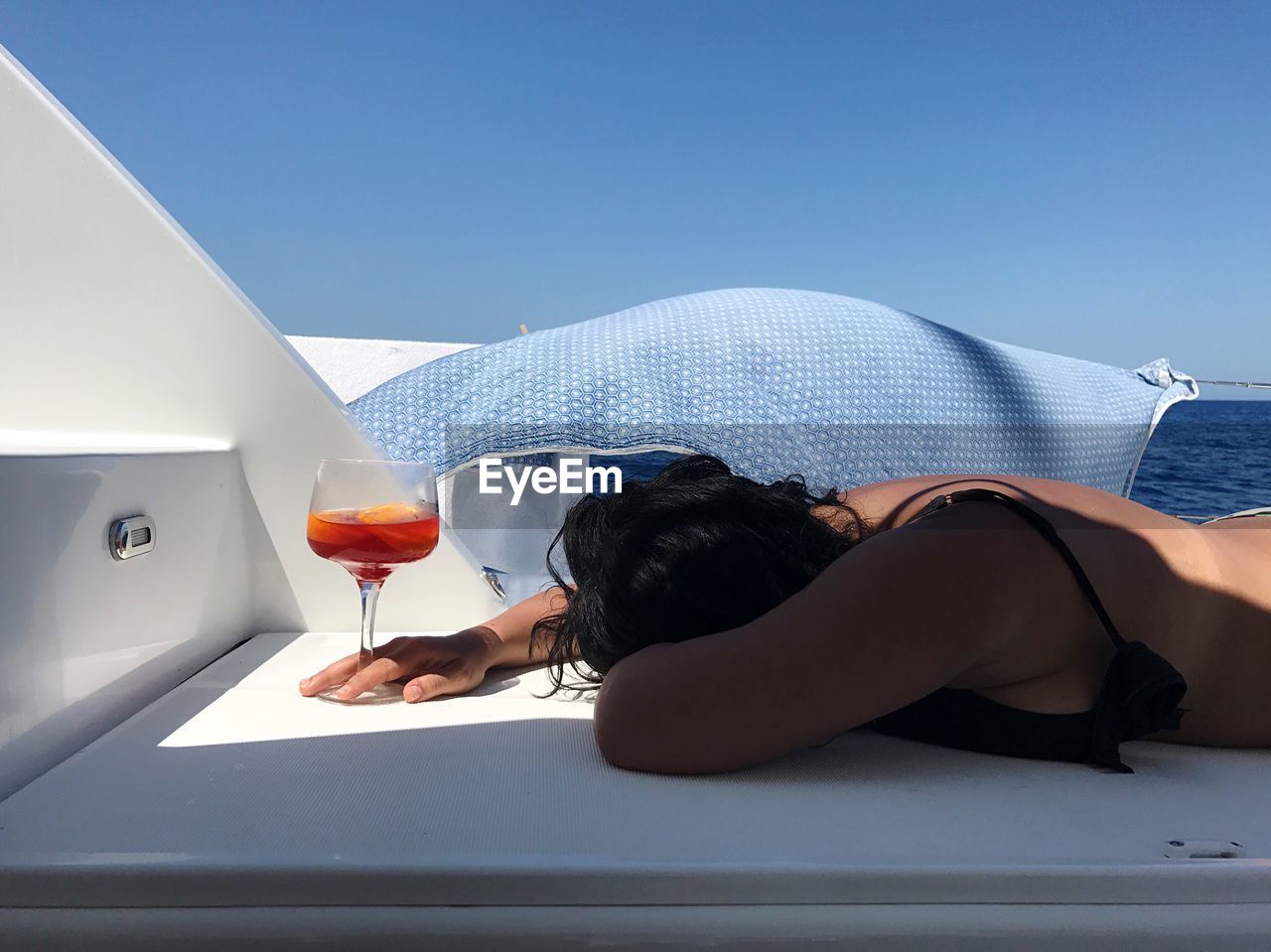 Woman with drink lying down on boat at beach against sky