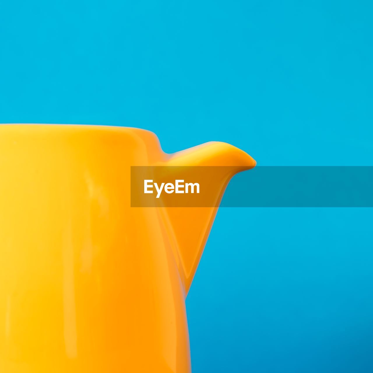 Close-up of yellow teapot against blue background
