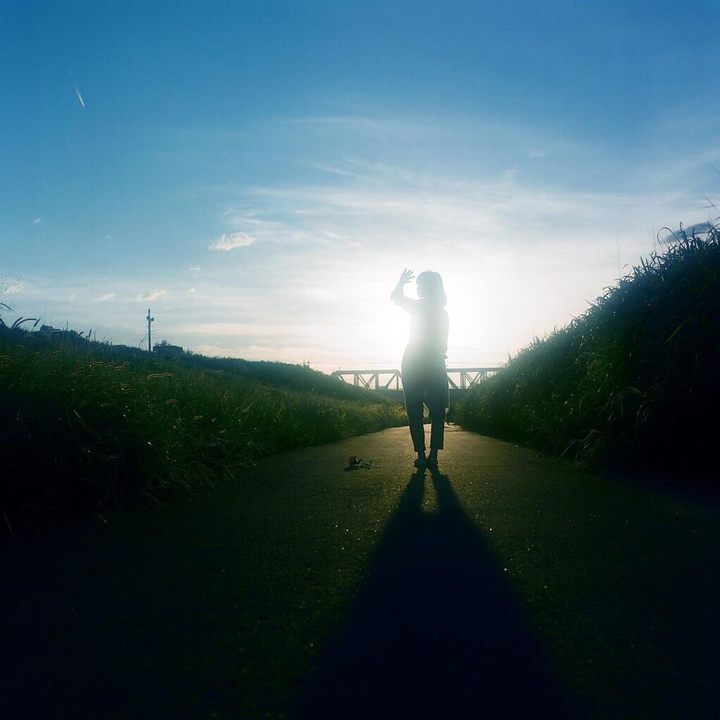 Rear view of a woman standing on country road against blue sky