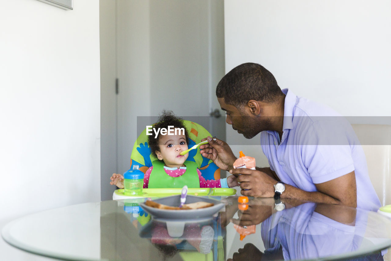 Father feeding daughter while sitting at table