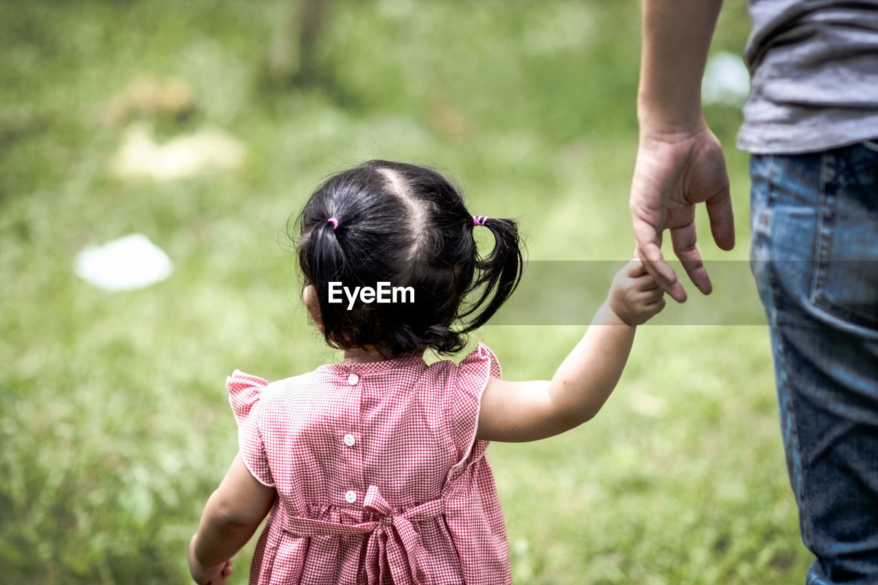 Midsection of father walking with little daughter at park