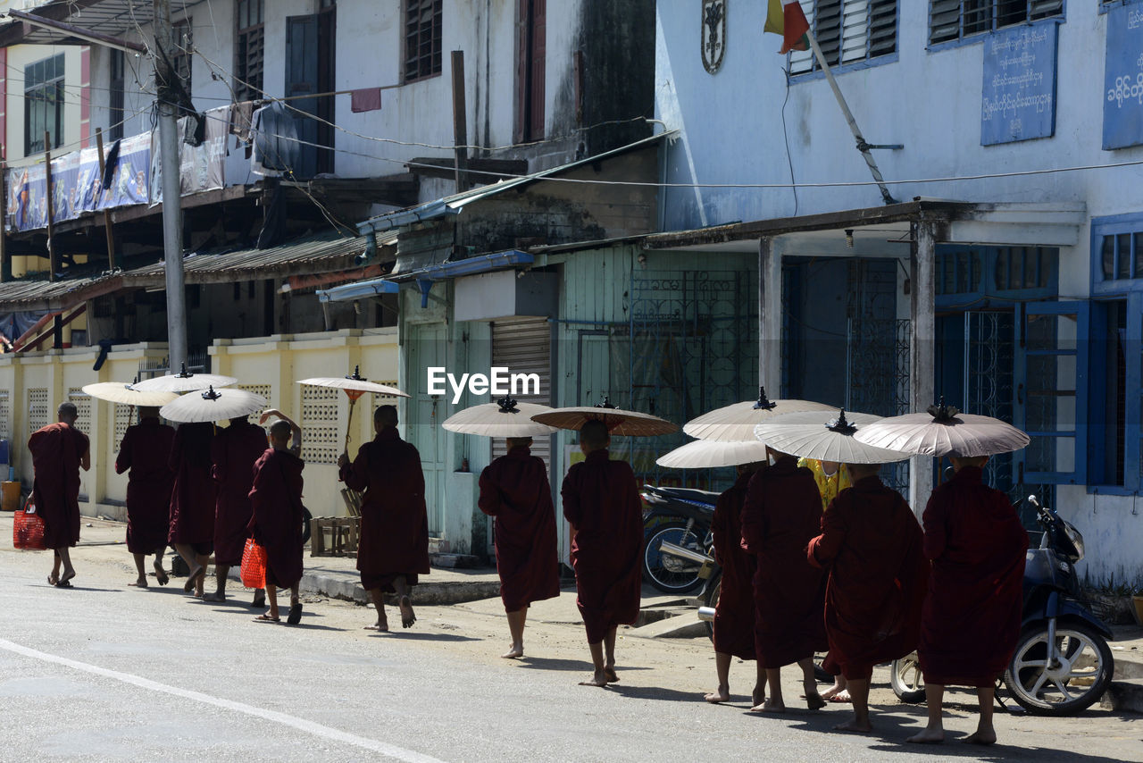 Monks walking on road by buildings during sunny day