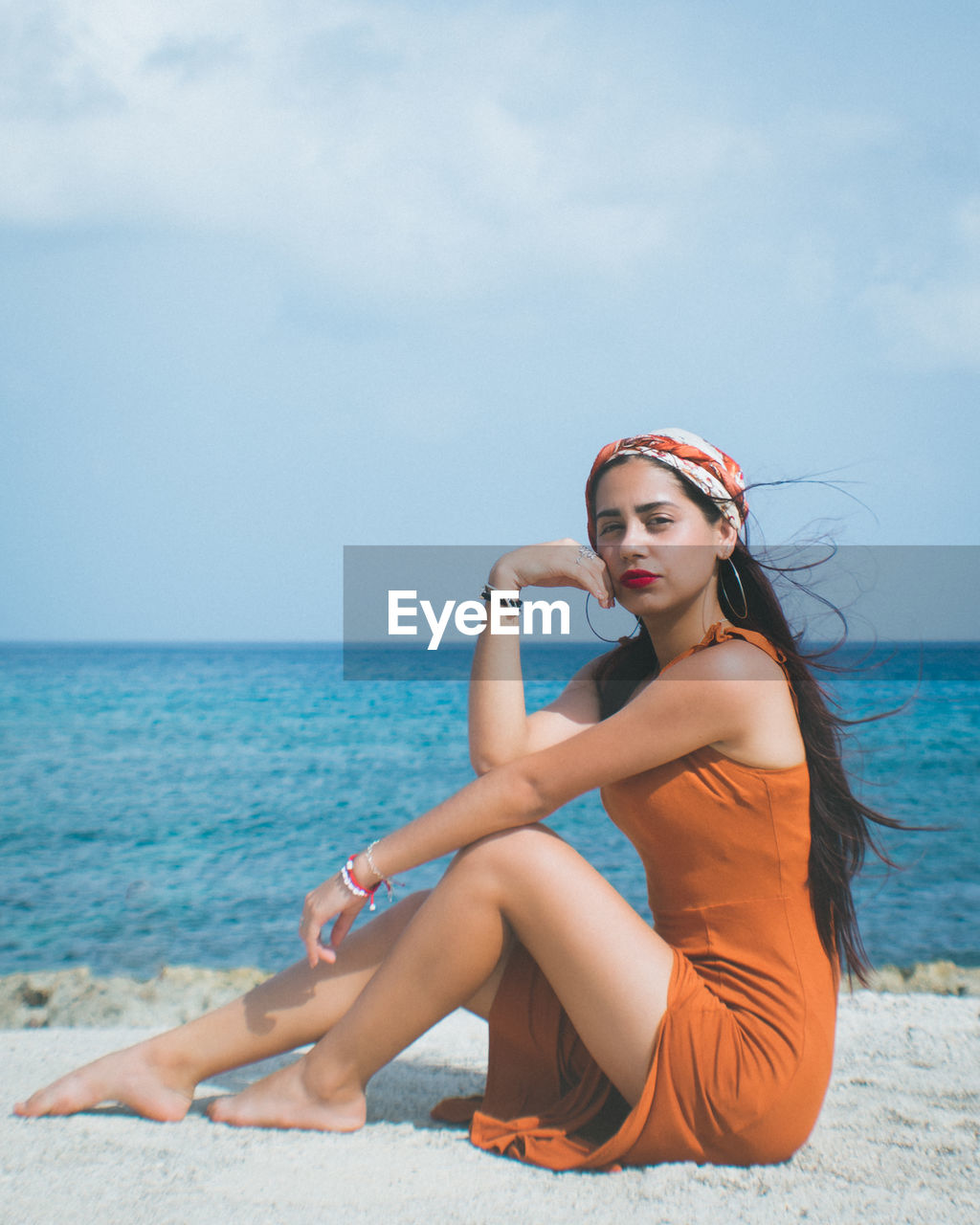 Young woman sitting on beach against sea