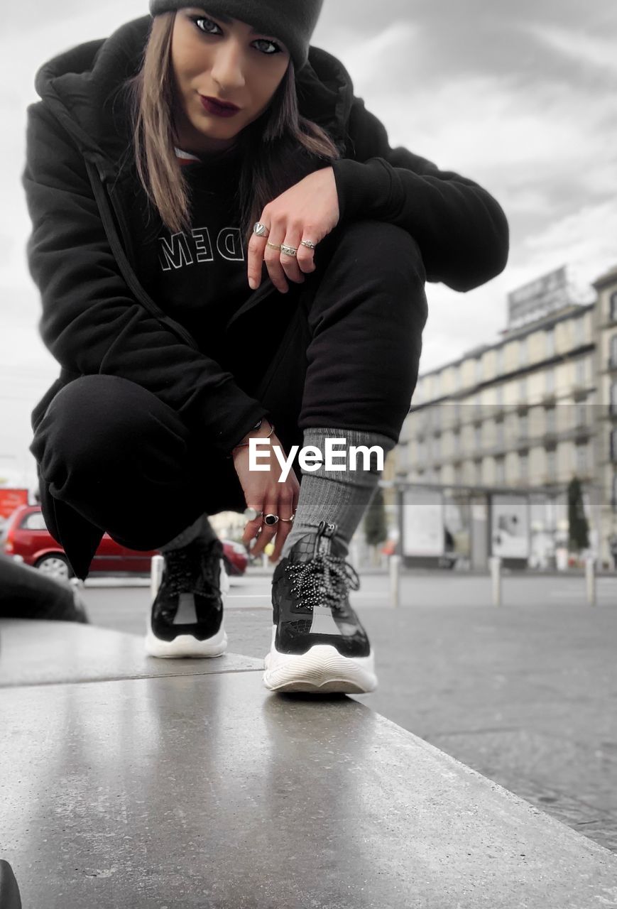 FULL LENGTH OF YOUNG WOMAN SITTING ON CITY