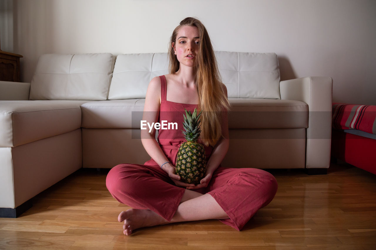 PORTRAIT OF A YOUNG WOMAN SITTING ON SOFA